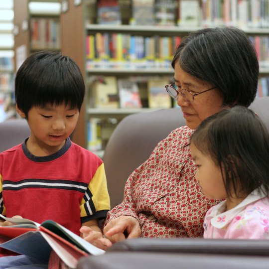 73_9282_11Dec2024135720_Grandmother reading a book with two children listening 540px.png